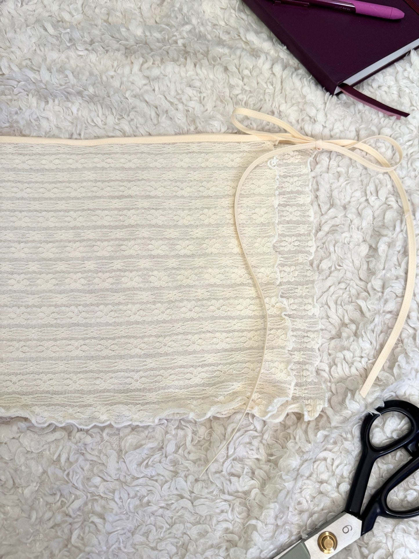 White lace skirt on a textured surface, with scissors and a notebook in the background.