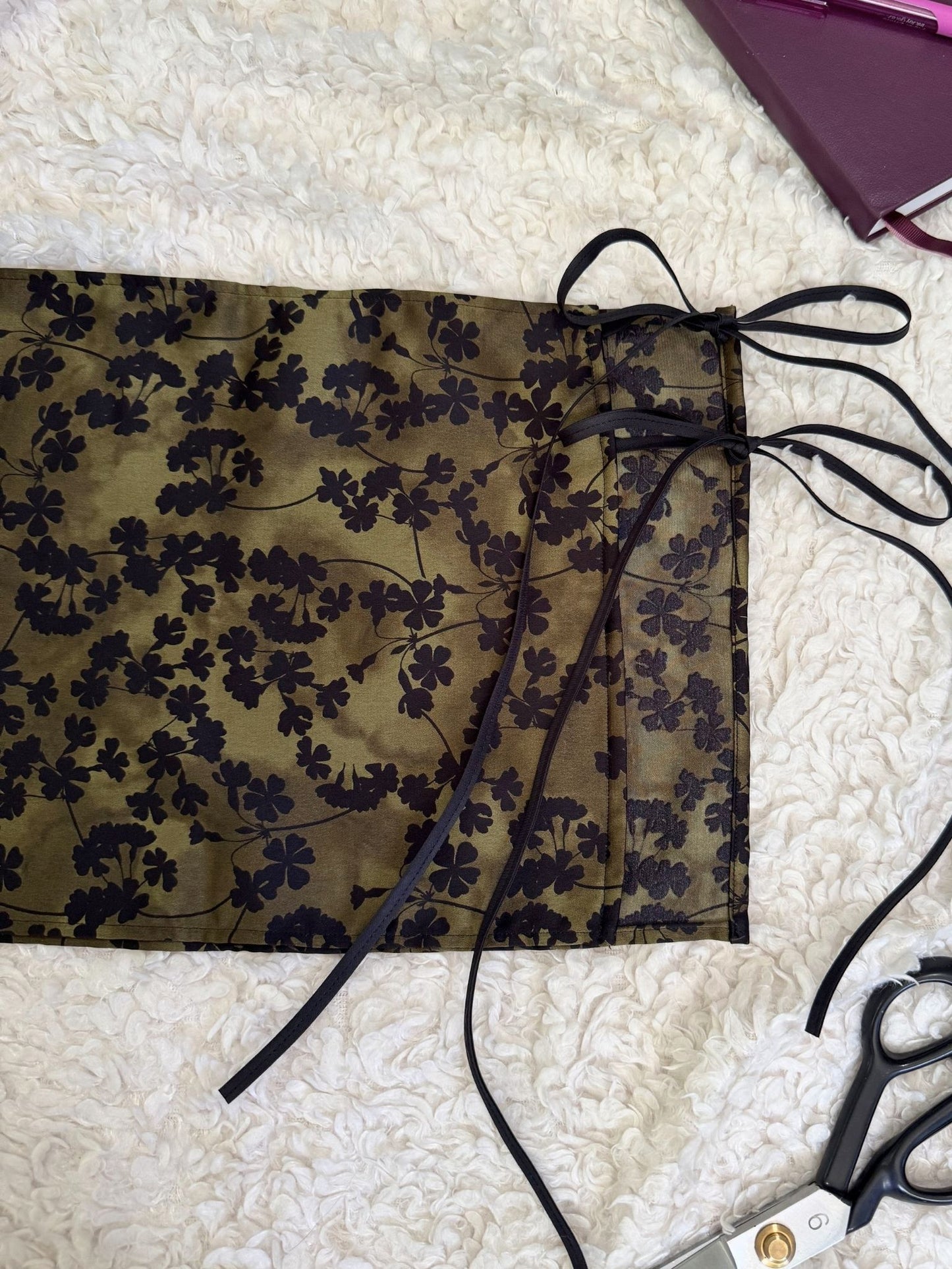 Green floral skirt with ties on a textured white surface with scissors.