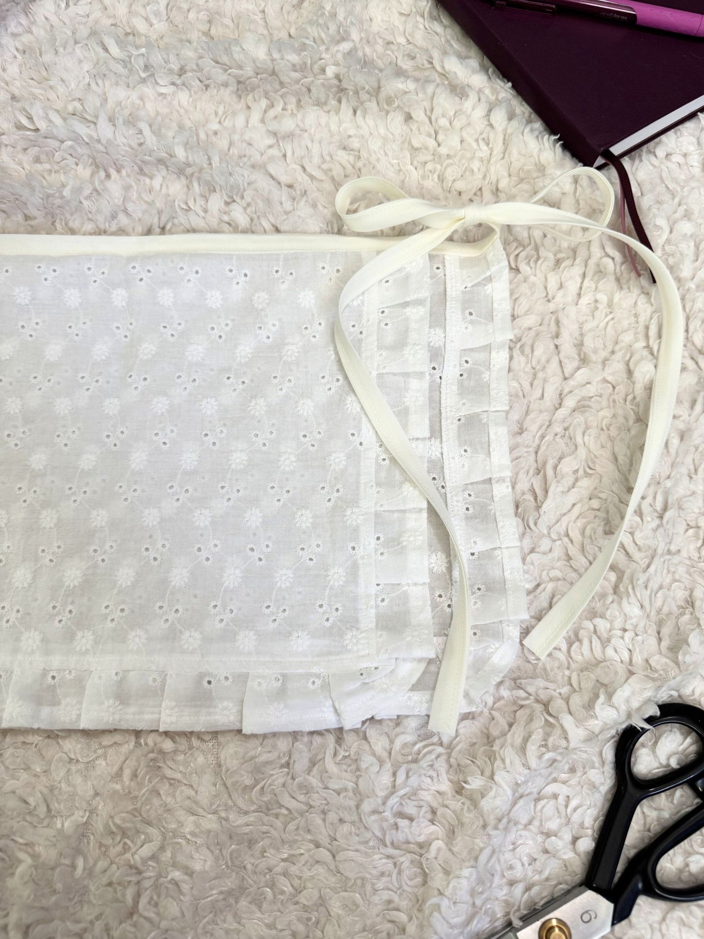 White lace fabric on a textured surface with scissors and a pen in the background