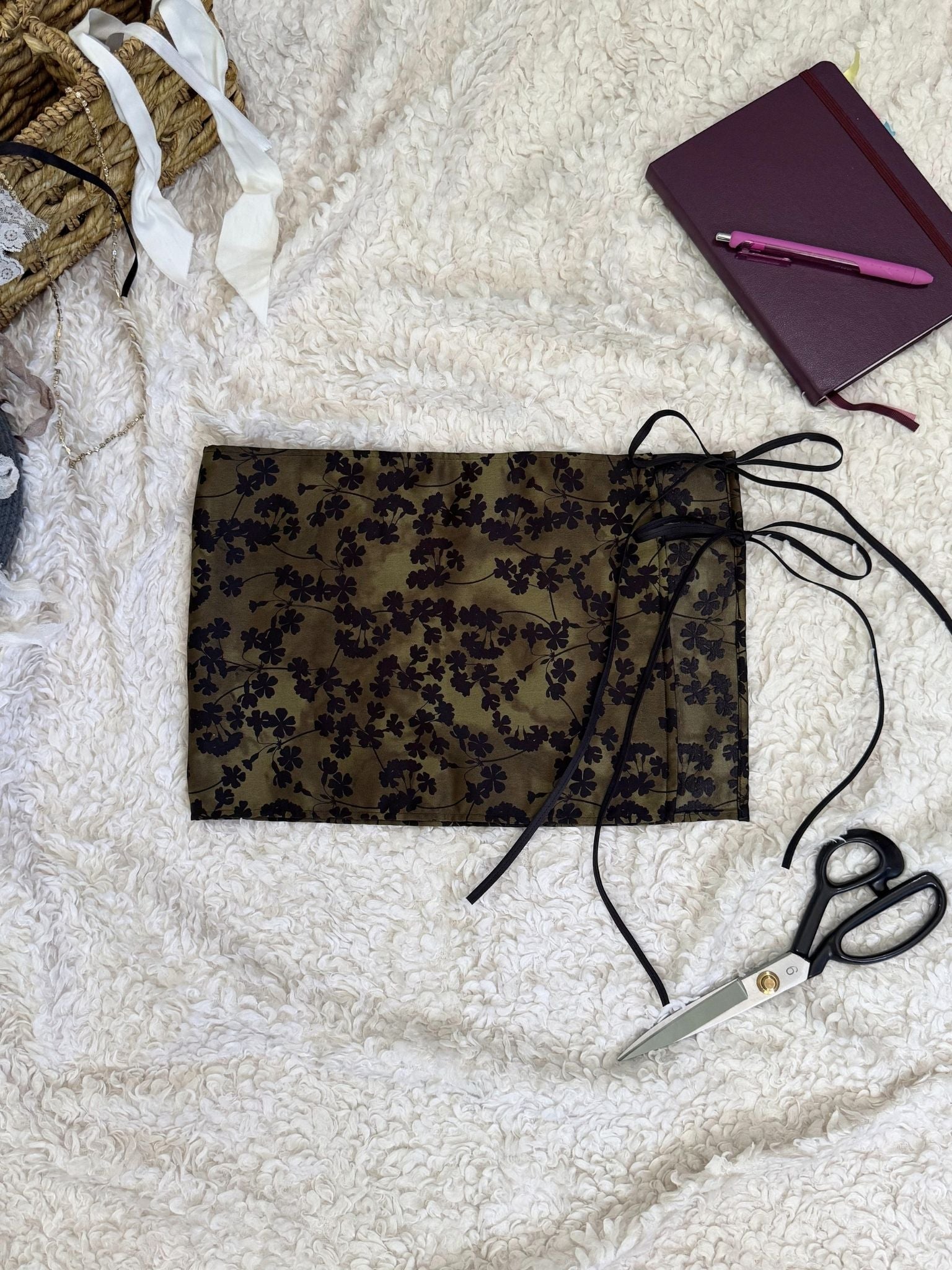 Green floral skirt with scissors and notebook on a textured white surface