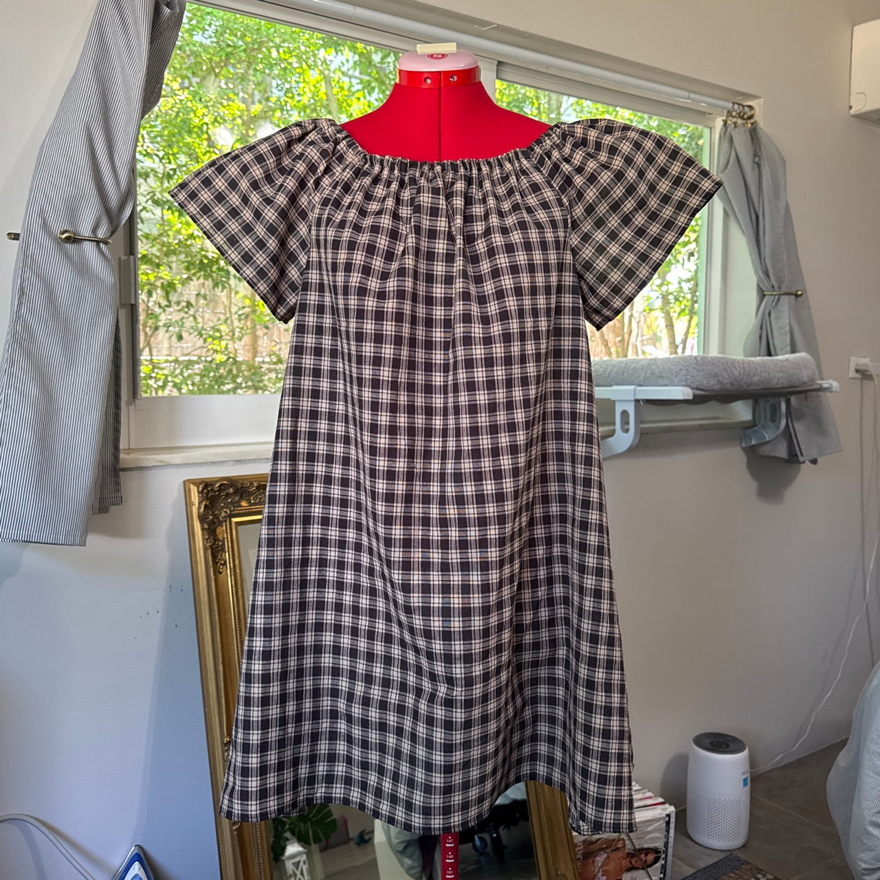 Plaid dress on a mannequin in a room with a window.
