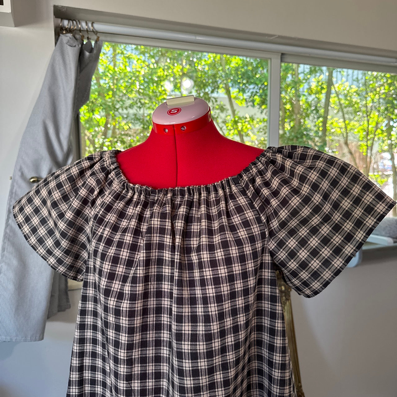 Black and white plaid dress on a mannequin in front of a window with greenery outside.