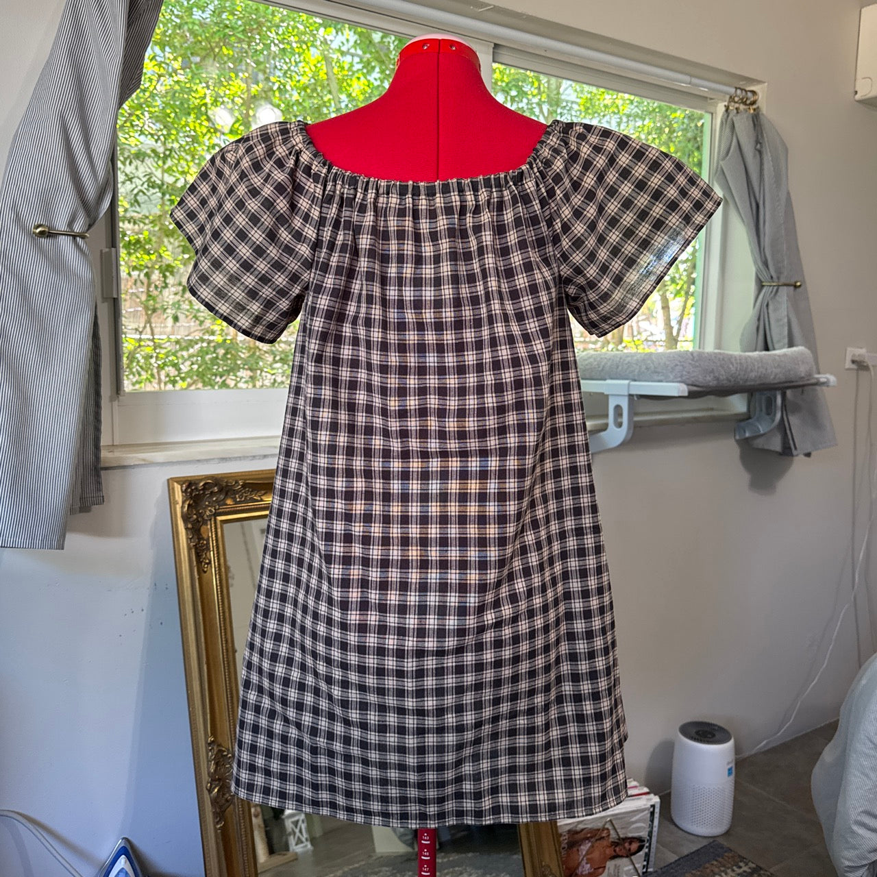 Plaid dress on a mannequin in a room with a window.