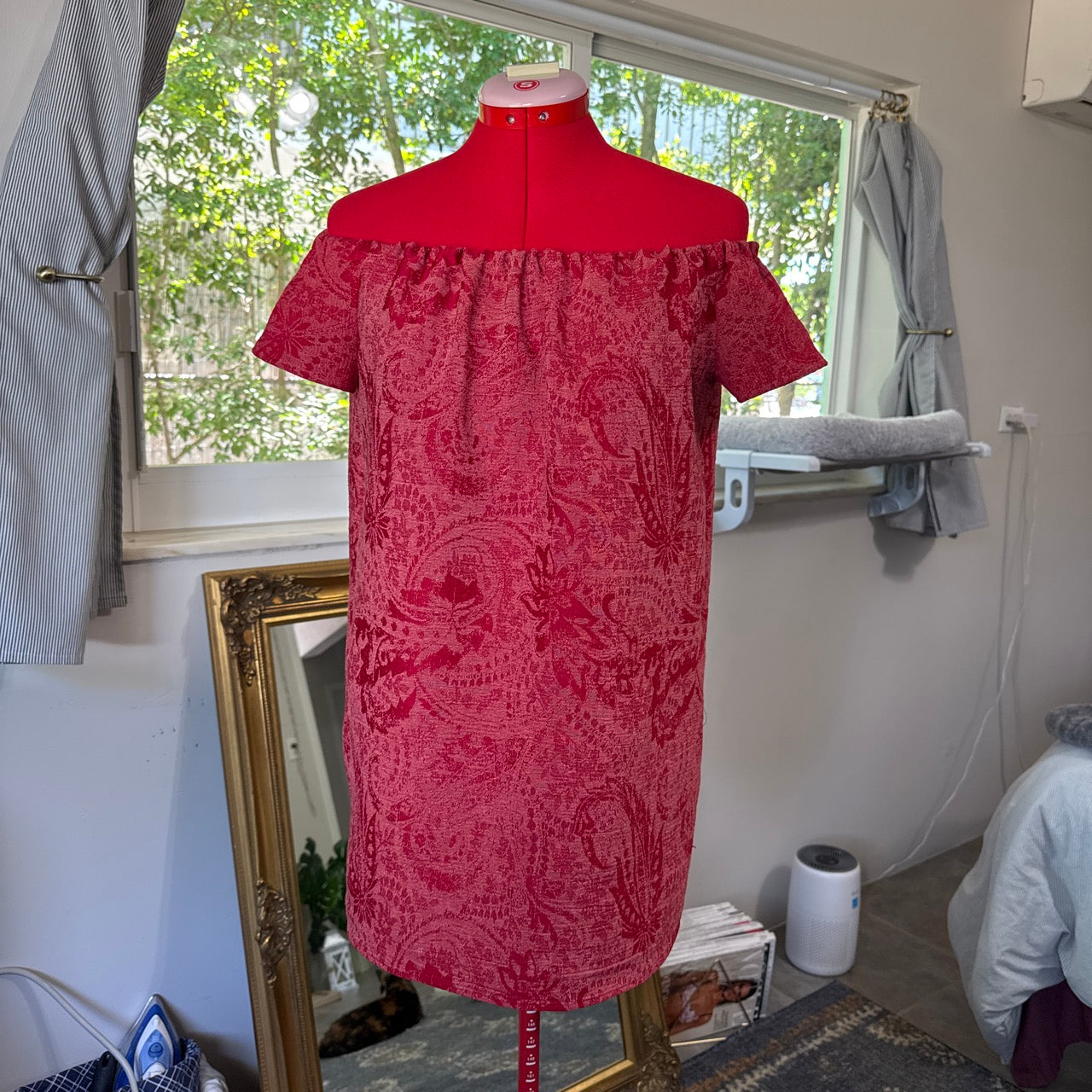 Red patterned dress on a mannequin in a room with a window.