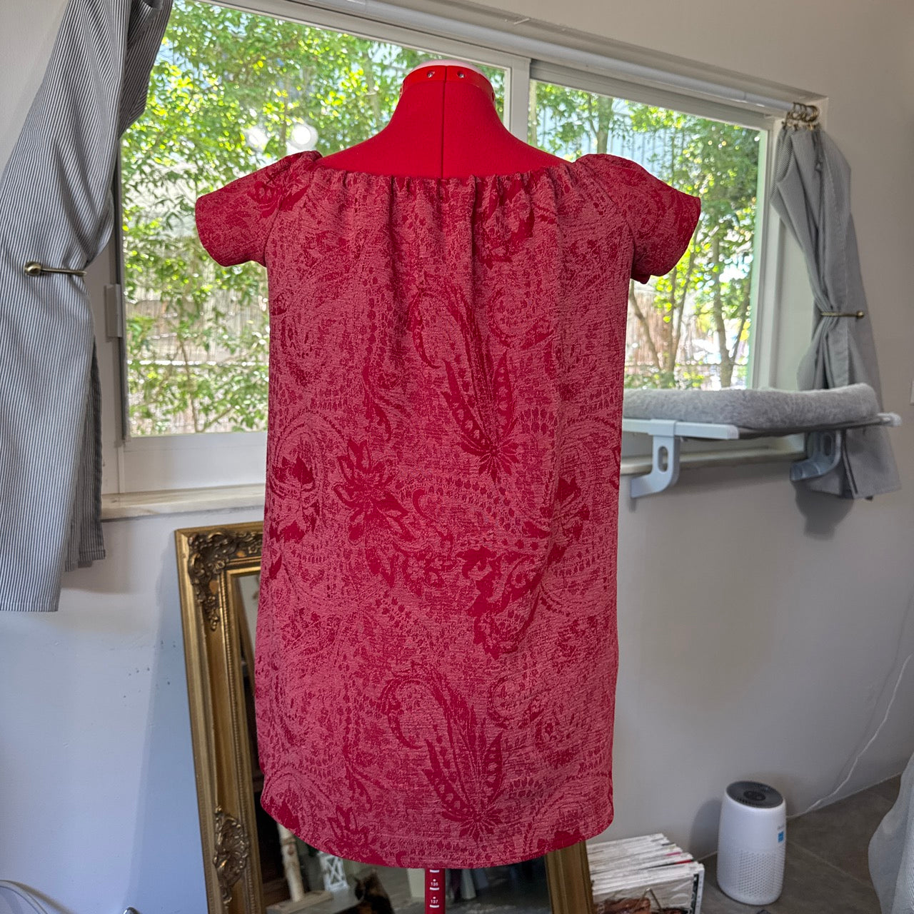 Red patterned dress on a mannequin in a room with a window.