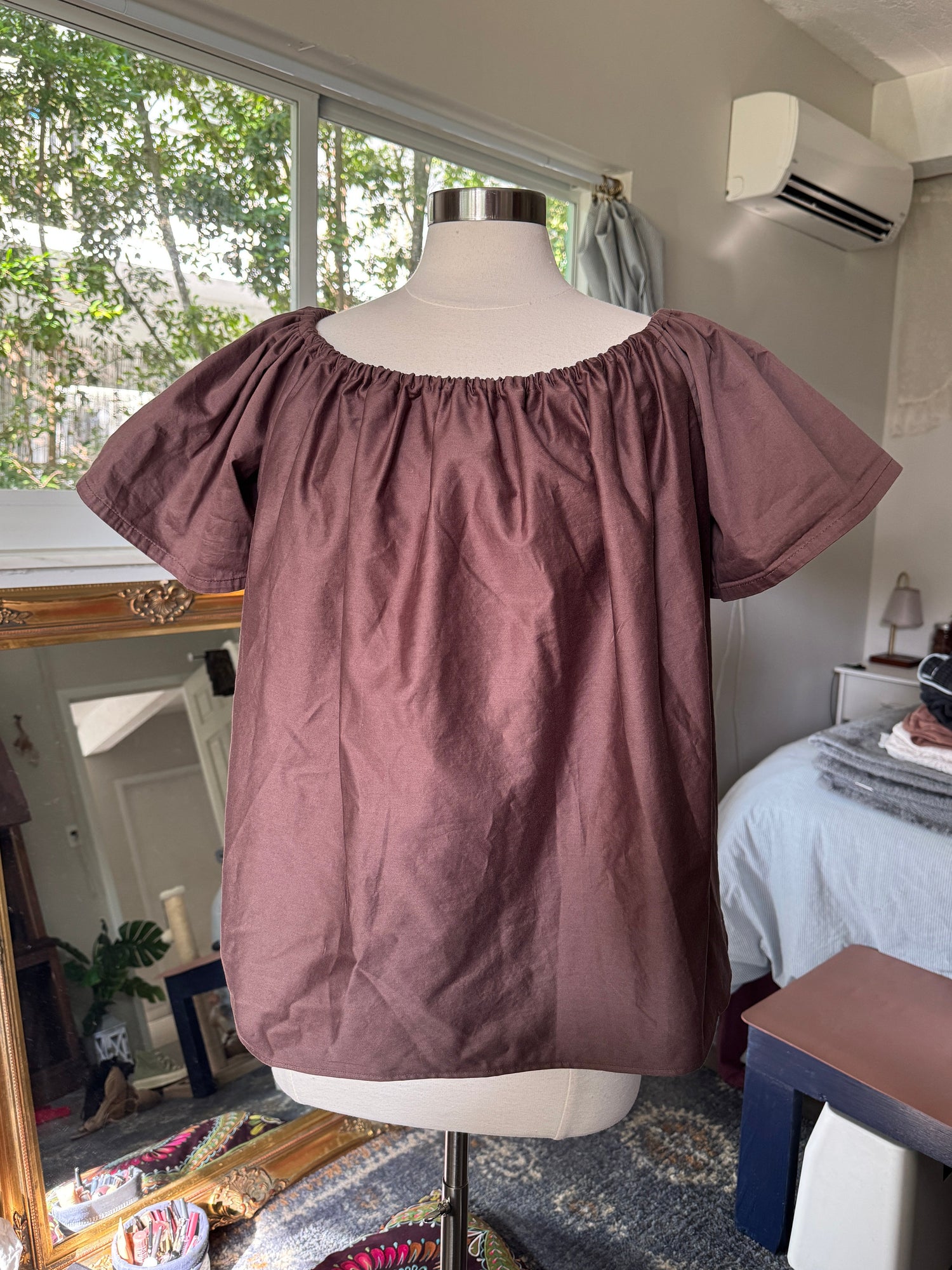 Brown blouse on a mannequin in a room with a window and air conditioner.