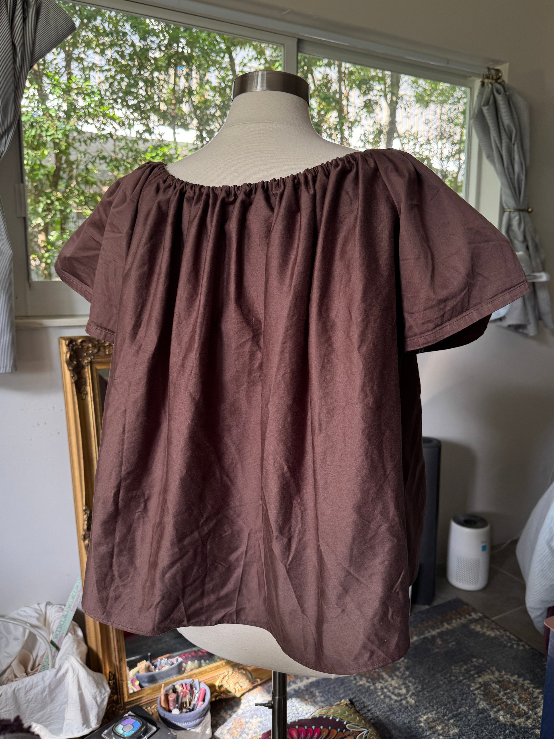 Brown blouse on a mannequin in a room with a window and curtains.