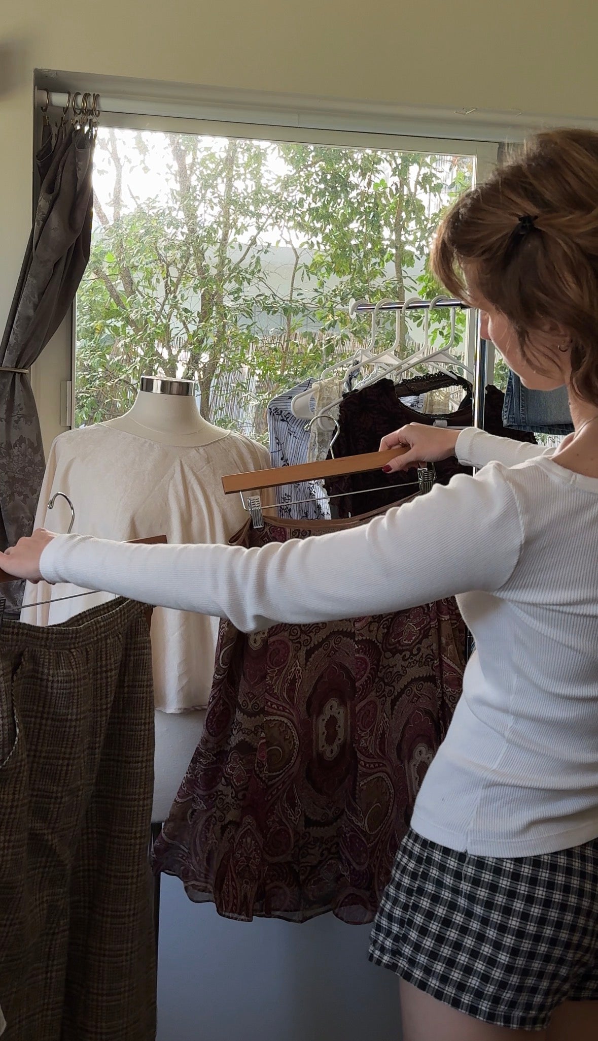 Person adjusting a garment on a mannequin in a room with large windows.