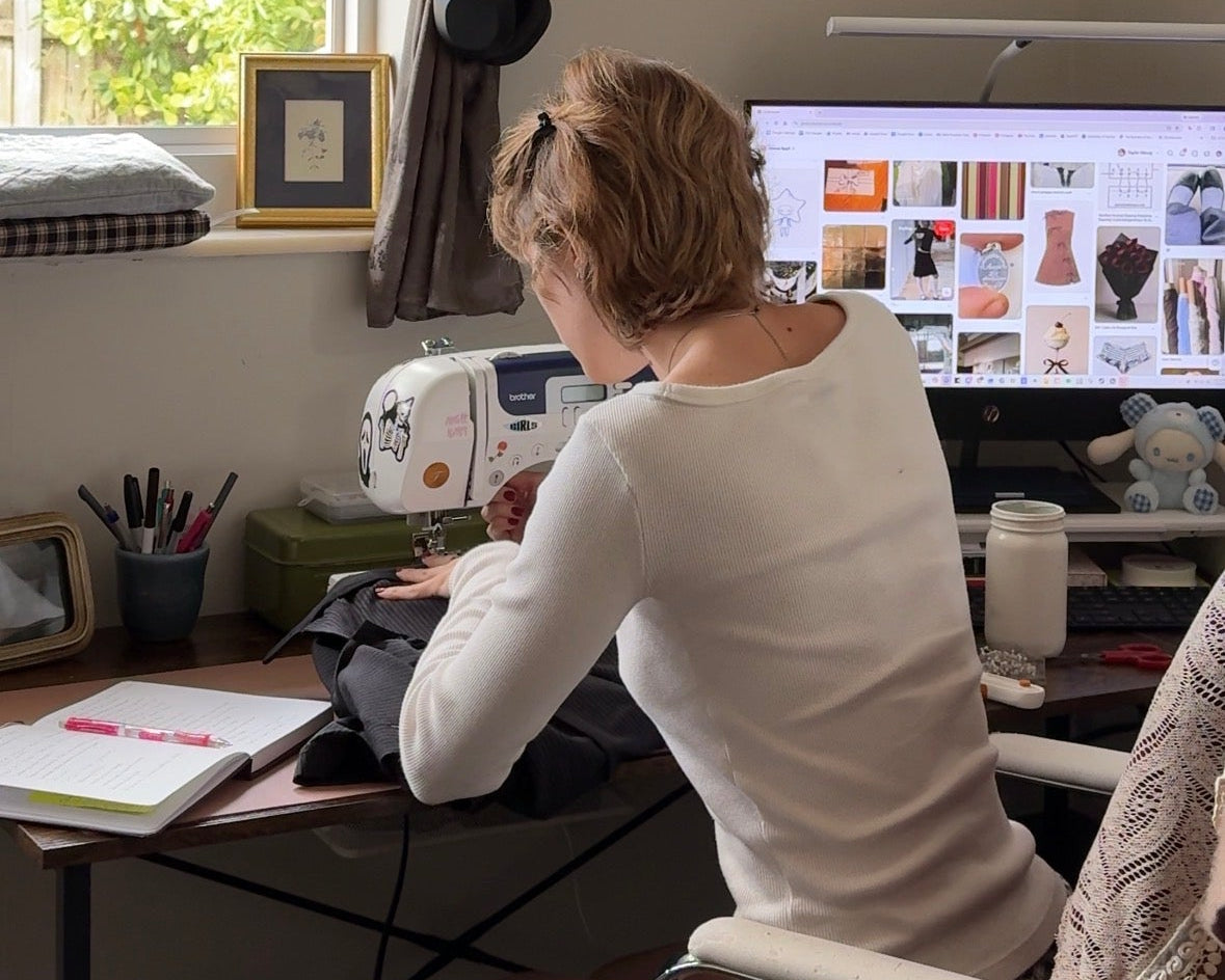 Person working at a desk with a sewing machine and computer displaying design software.